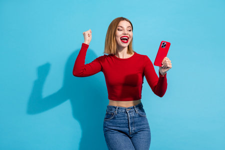 Lovely young woman celebrating with a bright red smartphone, radiating happiness and charm against a...