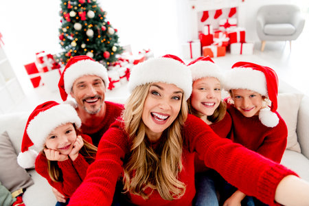 Family celebration Christmas selfie in a cozy living room with tree gifts Santa hats and warm...