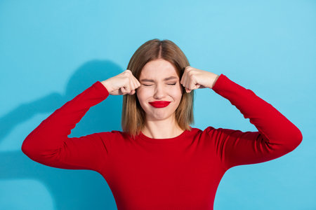 Young woman in a red top posing playfully against a vibrant blue background, showing expressive...