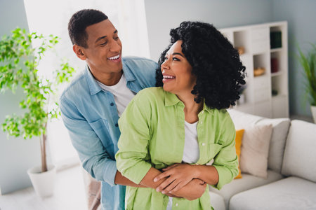 Photo of sweet excited couple dressed casual outfits having fun hugging together indoors house roomの写真素材