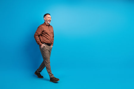 Confident mature businessman walks with style against a blue backdrop exuding professional leadership and corporate appealの写真素材