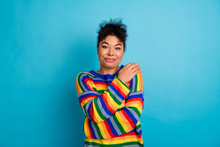 Young woman in rainbow striped sweater smiles against blue background for casual fashion lifestyle stock photoの写真素材