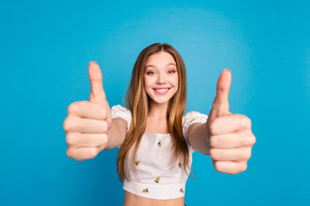 Photo of happy positive girl show in camera thumb up sign isolated blue color backgroundの写真素材