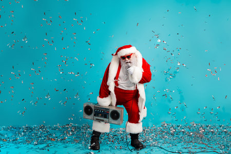 Santa performs a lively party with a boombox confetti and bright blue backdrop for a festive season photo shootの写真素材