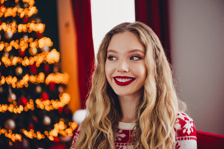 Joyful Christmas moment a smiling woman in a red sweater beside a twinkling Christmas tree at homeの写真素材