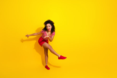 Cheerful woman in red striking a playful pose against yellow background, expressing joy and energy in stylish fashion.の写真素材