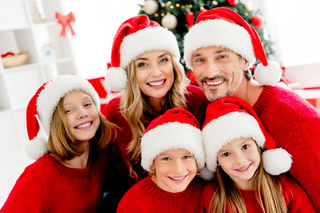Family celebration at Christmas time with parents and children in red sweaters and Santa hats in a cozy home setting by the Christmas treeの写真素材