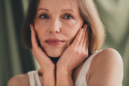 Unretouched portrait of pretty old woman touch face feel tenderness isolated green color linen backgroundの写真素材