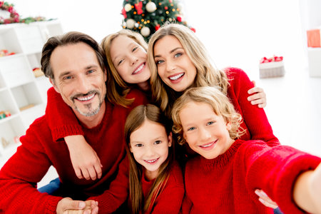 Family joy by the Christmas tree smiling together in a cozy home scene with parents and children in red sweaters during festive holiday seasonの写真素材