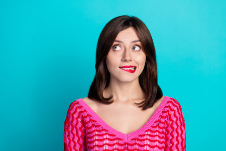 Portrait of lovely adorable girl with stylish hair wear pink top look at offer empty space biting lip isolated on blue color backgroundの写真素材