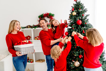 Family gathers at home decorate Christmas tree together in cozy holiday scene parents children and friends wearing sweaters sharing joyの写真素材