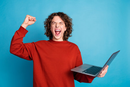 Photo of funky lucky guy dressed red pullover winning game modern gadget isolated blue color backgroundの写真素材