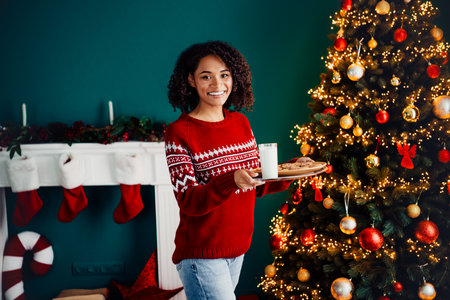 Bright Christmas hostess serves cookies and milk beside a glowing tree in a cozy home scene full of joy and festive warmthの写真素材