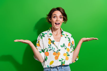 Photo of cheerful excited girl two arm demonstrate empty space recommend buy nice quality product isolated on green color backgroundの写真素材