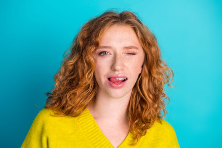Bright portrait of a young redhead woman in a vivid yellow sweater, winking playfully against a...