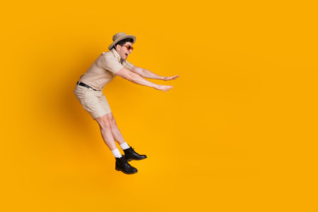 A young man in safari attire leaps playfully against a bold orange background conveying adventure...