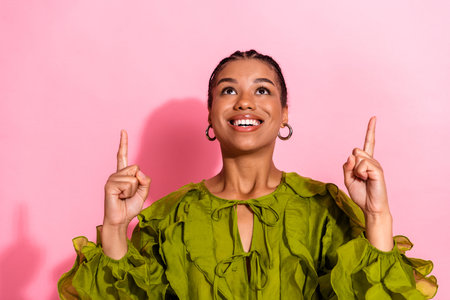 A smiling young African American woman in a vivid green blouse lifts both index fingers toward the...