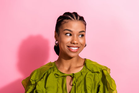 A cheerful young African American woman in a vivid green blouse smiles against a pink background,...
