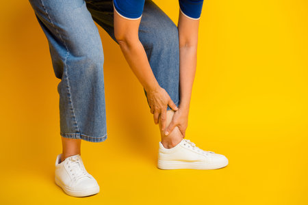 A casual stylish scene featuring a woman in jeans and white sneakers bending to tie her shoelace against a bold yellow backdrop, conveying everyday comfort and fashion for lifestyle and retail use.