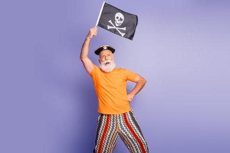 A mature man in a bright orange tee and zigzag striped pants stands on a purple backdrop, waving a pirate flag.