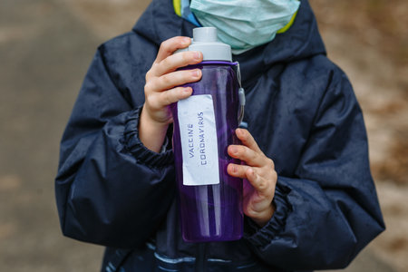 A child in a medical mask holds a bottle with the inscription  coronavirus vaccine