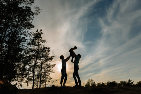 The silhouette of a father and mother raising their son above them against the background of the sunsetの写真素材