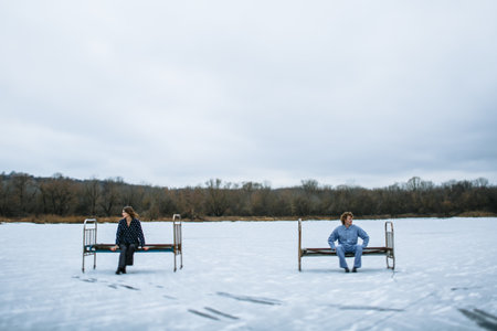 A guy and a girl in pajamas are on the ice of a frozen lake. People sit on an iron bed on the ice.の写真素材