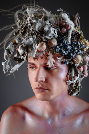 The face of a male model in a headdress of fresh flowers filled with wax. The person's face is covered with sequinsの写真素材