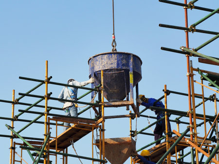 Construction workers working on scaffolding with blue sky at construction siteの写真素材