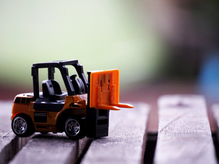 Miniature yellow forklift model on wooden table. Warehouse logistics business or construction...