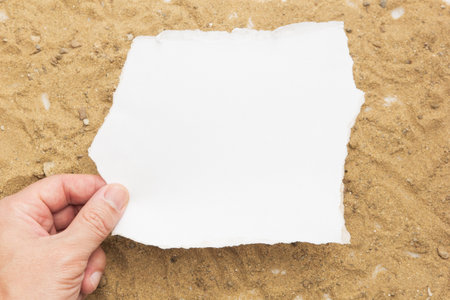 Concept hand holding a blank white paper on a brown sand background,blank paper for your letter.