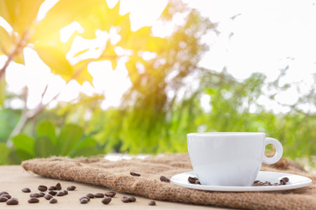 White coffee cup with coasters and coffee beans placed on brown burlap cloth on natural background.の写真素材