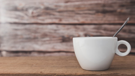 A white coffee cup with a spoon in the cup is placed on a wooden plate and on a wooden background.の写真素材