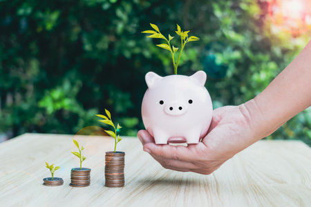 Close up of male hand stacking coins and hold pikkybank with green bokeh background,Save money for prepare in the future.Trees growing on coin,Business Finance and Money concept.の写真素材