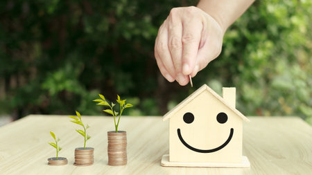 person putting coin on the piggybank on table, plant growing up on coin, business finance and saving money investment for buying a home,investing in real estate or property.の写真素材