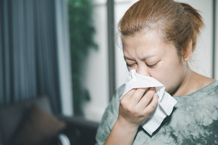 Sick woman sneezing and wiping nose with tissue in living room,feeling unhealthy and ill,There is a lot of dust. Allergies.Health care person on virus seasonal.の写真素材