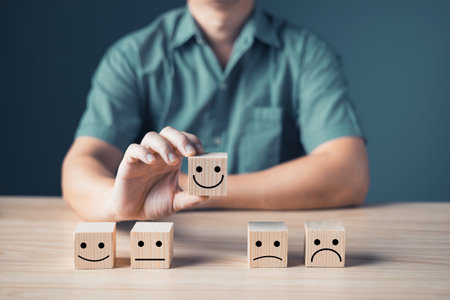 Hand of a businessman chooses a smile face on wood block circle.Customer service experience and business satisfaction survey.rating very impressed.Satisfaction survey concept.の写真素材