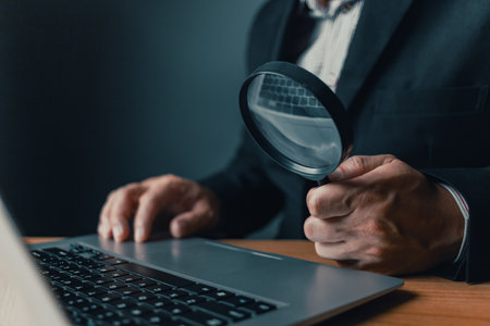 Businessman sit at office in suit holding magnifying glass and computer laptop.Search and research concept.の写真素材
