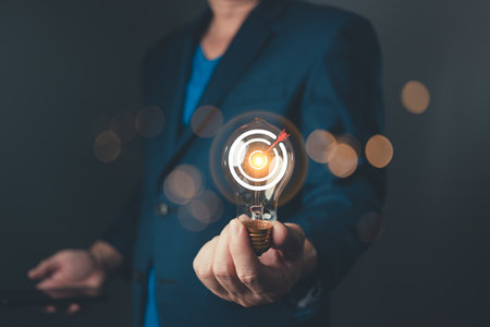 A professional hold glowing lightbulb with a target symbol, representing a business goal and strategic plan, showcasing innovation, focus, and determination for success in a competitive environment.の写真素材