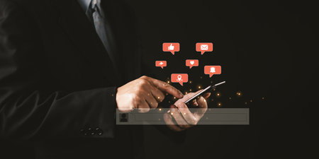 A person in a suit uses a smartphone as glowing red social media icons like, heart, location,...