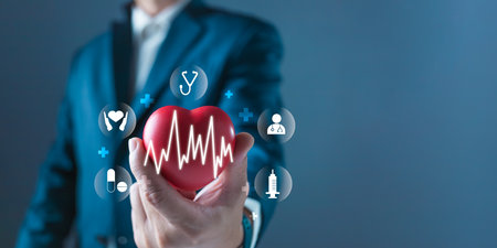 A person in a suit holds a heart with a pulse line overlay, surrounded by digital healthcare icons...