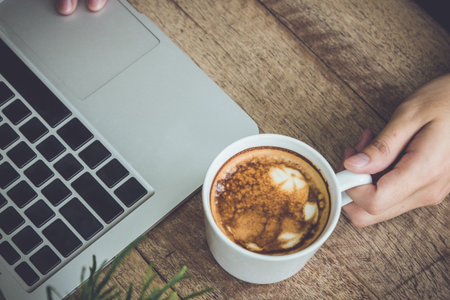 man using laptop and coffee cup on wood table ,vintage tone