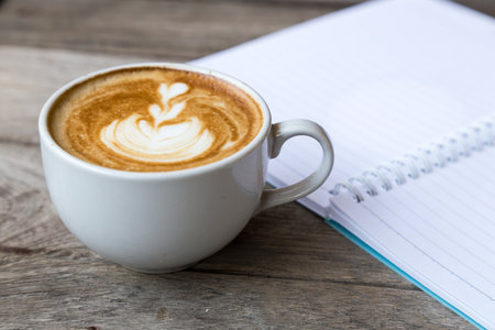 cup of latte coffee with notebook on wood table