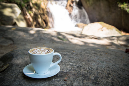 cup of coffee on stone with blur waterfall backgroundの写真素材