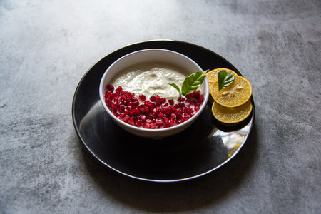 Pomegranate seeds and fresh yogurt in a bowl on a black plate