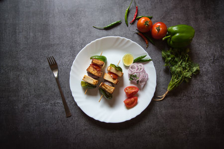 Top view of paneer tikka on a white plate along with salad and vegetable condimentsの写真素材