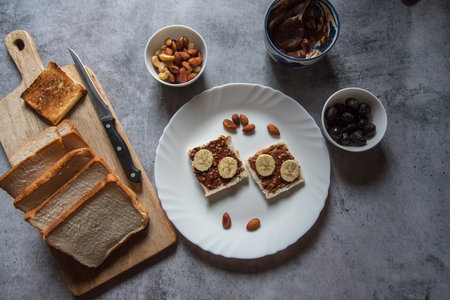 Top view of healthy breakfast food ingredients bread, peanut butter, bananas, almonds, nuts, dry fruits milk. Concept of wholesome and healthy food.の写真素材