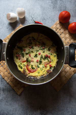 Traditional frittata an egg based Italian dish prepared in slow fire with ingredients of tomato cheese onion and chillies. Top view.の写真素材