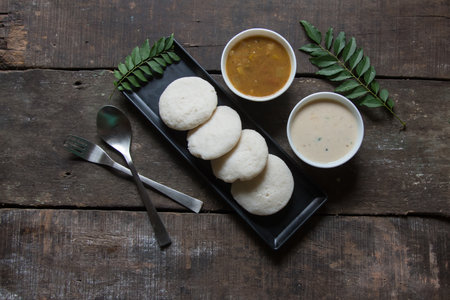 South Indian snacks idli sambar or idly sambhar prepared by steaming fermented rice and served with coconut dip and vegetable soup in a black tray. Top view.の写真素材