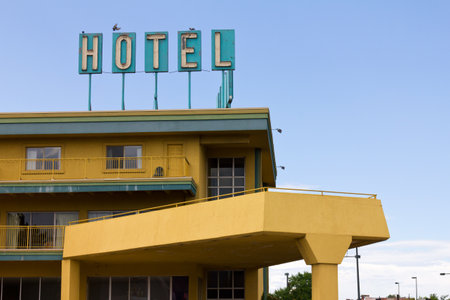 An old dirty hotel sign with birds perched on top stands above a colorful motel on the side of the highway.のeditorial素材